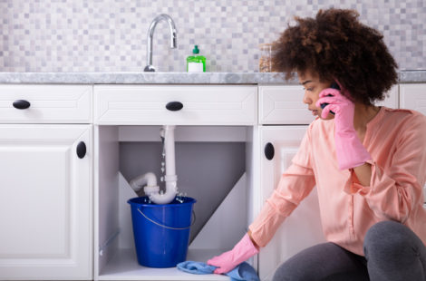Young Woman Wearing Pink Gloves In Hand Calling Plumber In Front Of Leaking Sink Pipe