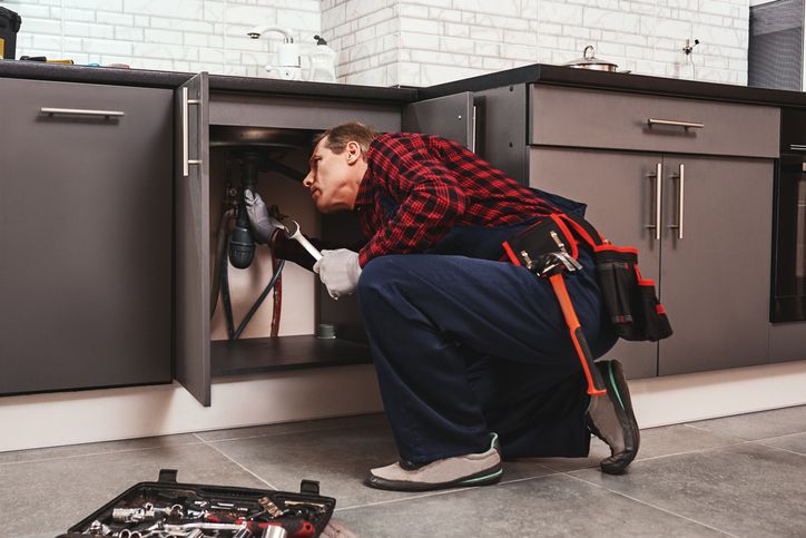 Man inspecting pipes under a sink