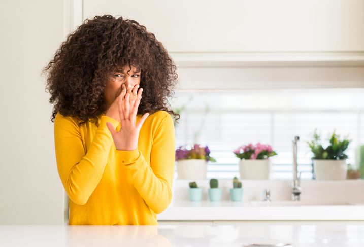 Woman standing in kitchen plugging her nose