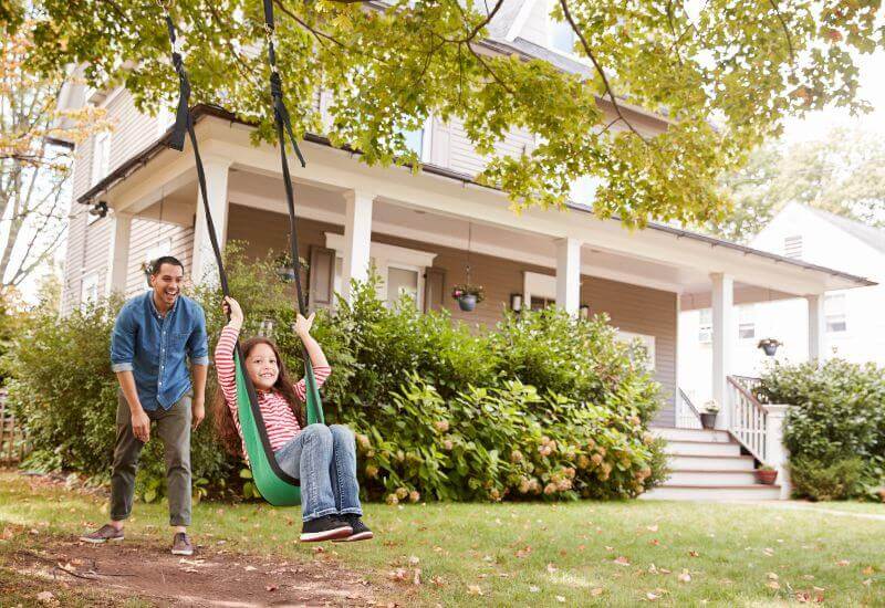 Father pushing daughter in garden swing