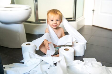 A Toddler ripping up toilet paper in bathroom