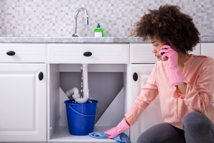 Young woman wearing pink gloves calling plumber about leaking sink