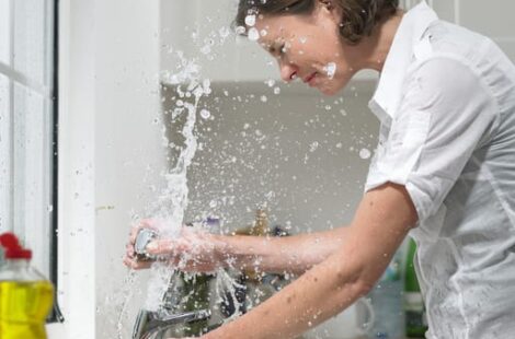 Woman getting splashed with water while fixing a kitchen sink